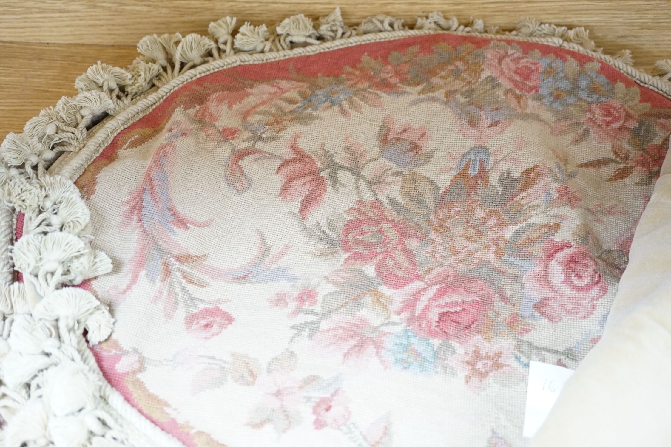 Four 20th century oval floral needlework cushion covers, design with sprays of roses in pastel colours, edged with a cream tasselling and velvet backing, 54cm wide